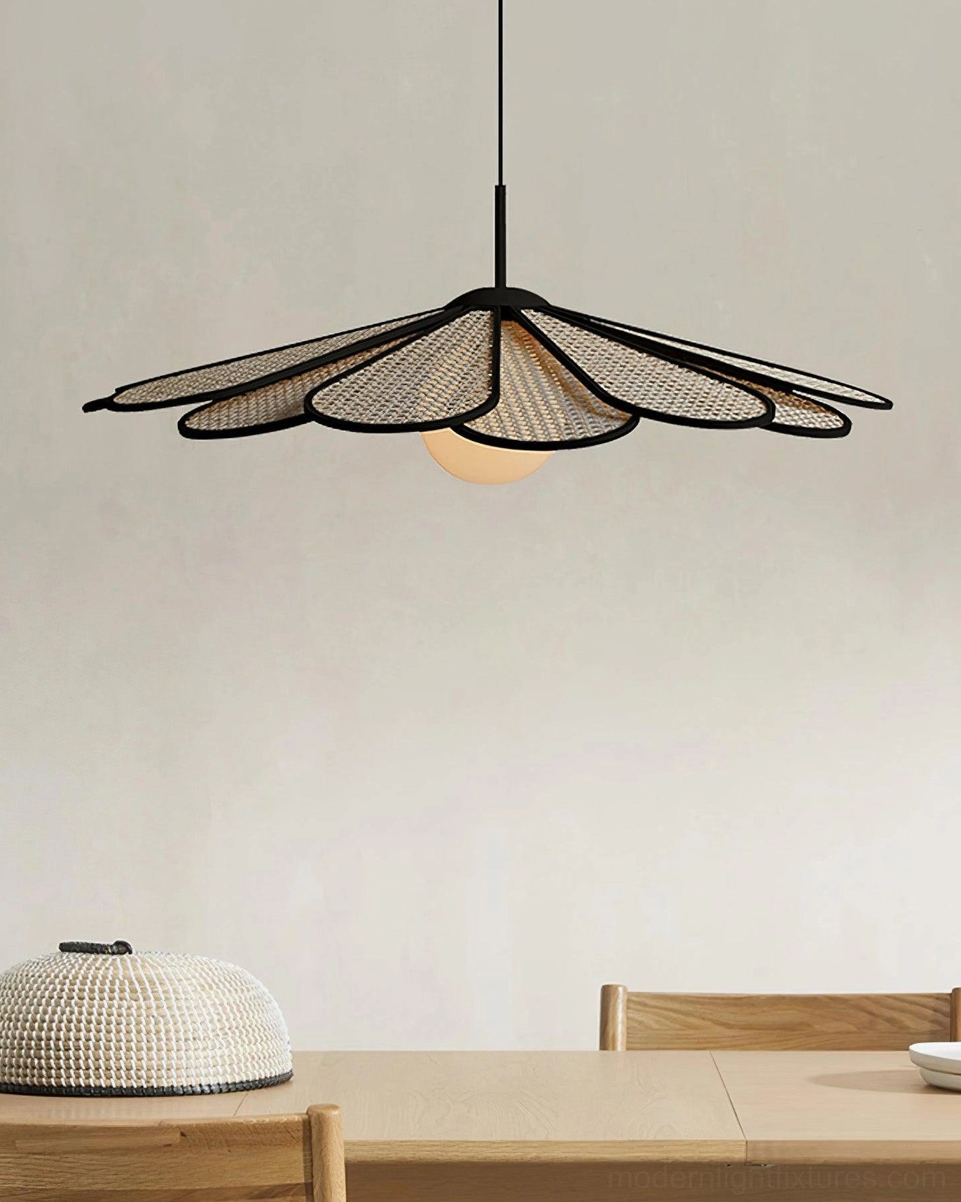 Woven rattan pendant lamp with black-trimmed flower shade in minimalist dining room interior setting