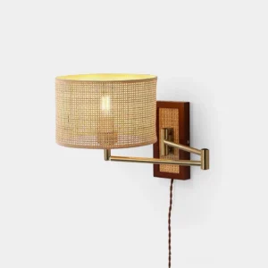 Rattan swing arm wall sconce with brass metal arm and wood base on plain white background, front flat view