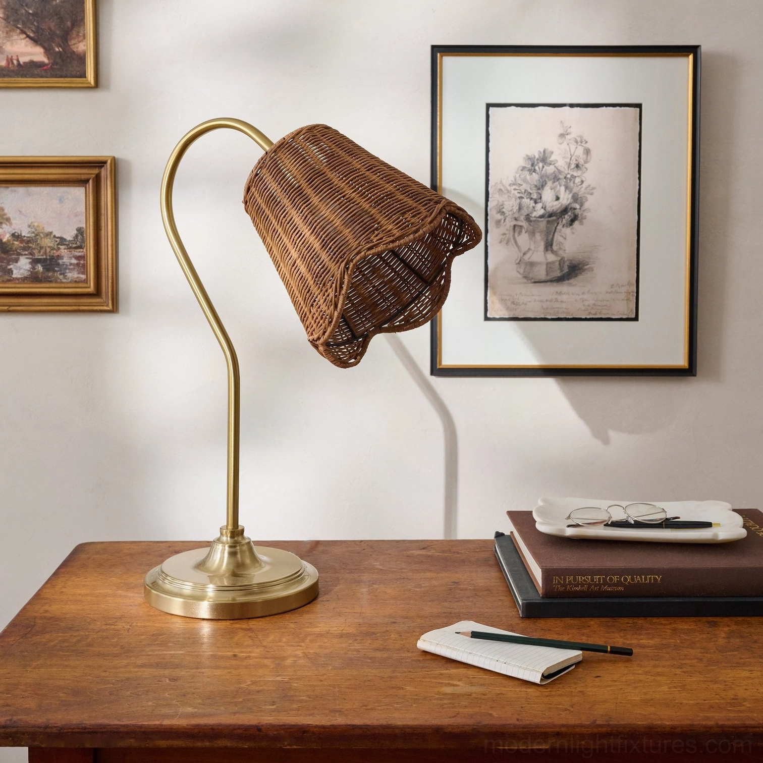 Brass base rattan table lamp on wooden desk with framed wall art and stationery home office setup