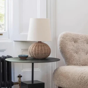 Rattan table lamp styled in modern living room interior, placed on black side table with tufted armchair and radiator in background
