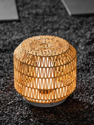 Close-up top-front view of woven rattan outdoor lantern lamp on gravel patio with warm illumination
