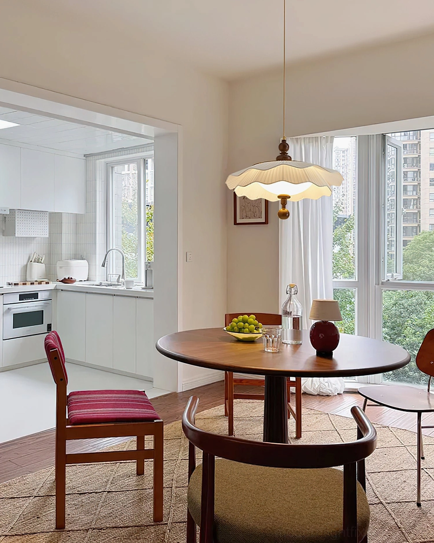 Ravina pleated pendant light suspended over round wooden dining table in open-concept home setting