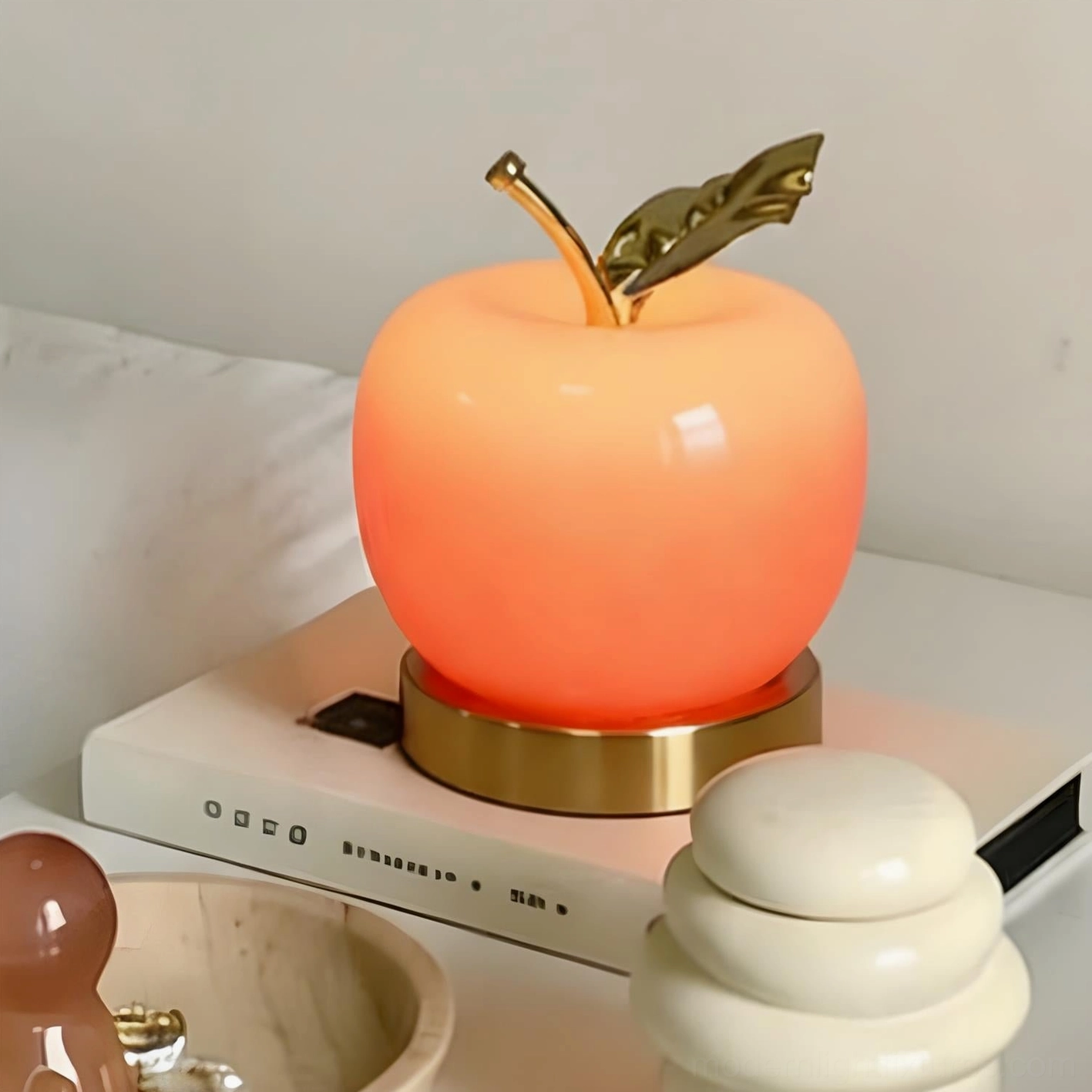 Red apple shaped table lamp with gradient finish, lit from inside showing warm ambient light on bedside table