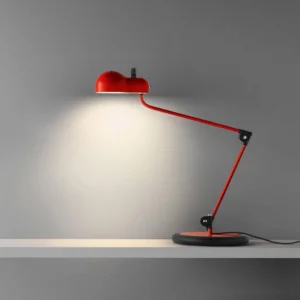 Red metal articulated table lamp with articulated joints displayed on interior floating shelf with warm spotlight effect