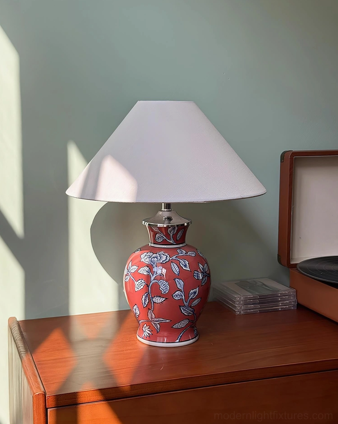 Red ceramic table lamp with white floral pattern and fabric shade, wooden side table with vinyl player accessories