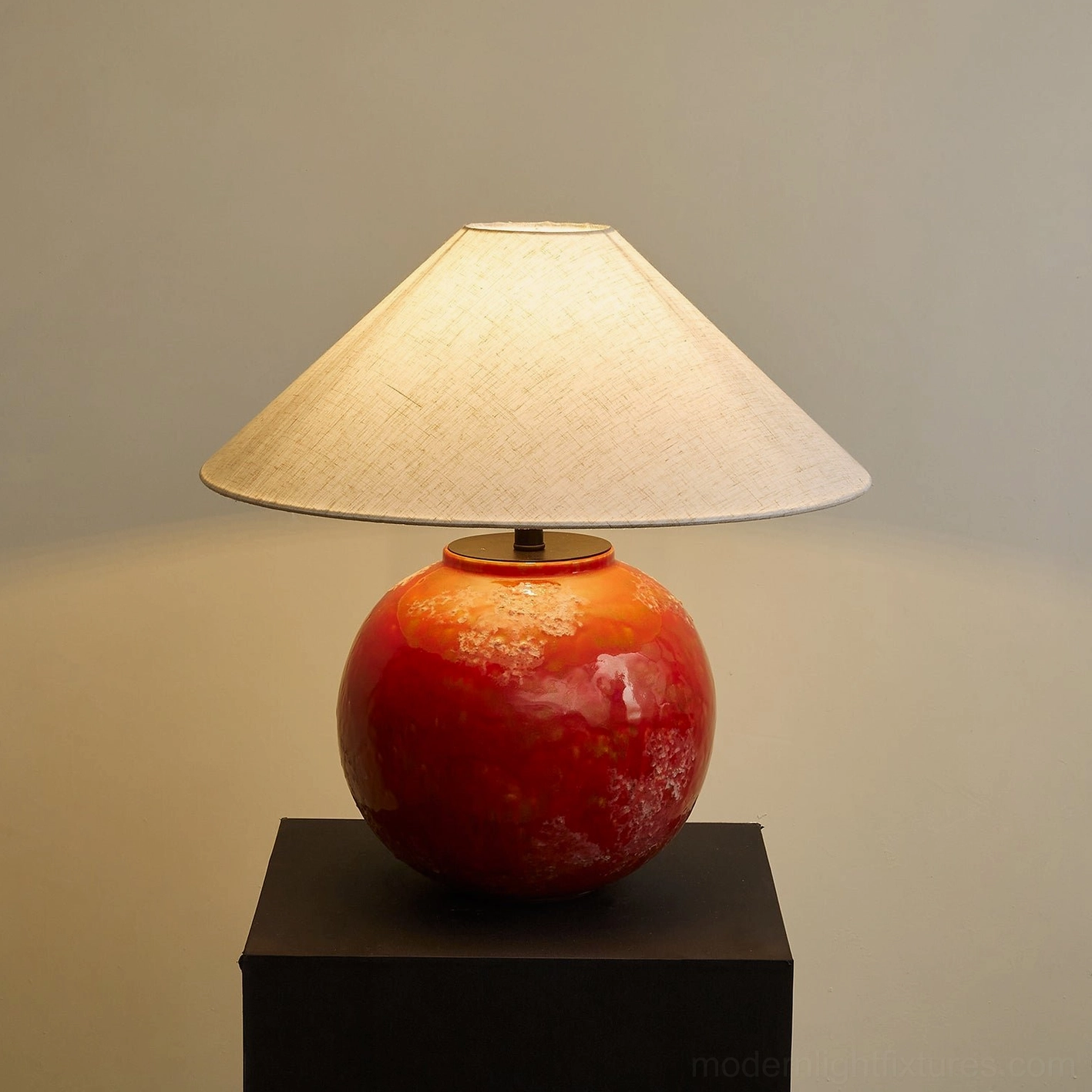 Hand-finished red marbled ceramic table lamp base with linen shade emitting warm ambient light in studio setting