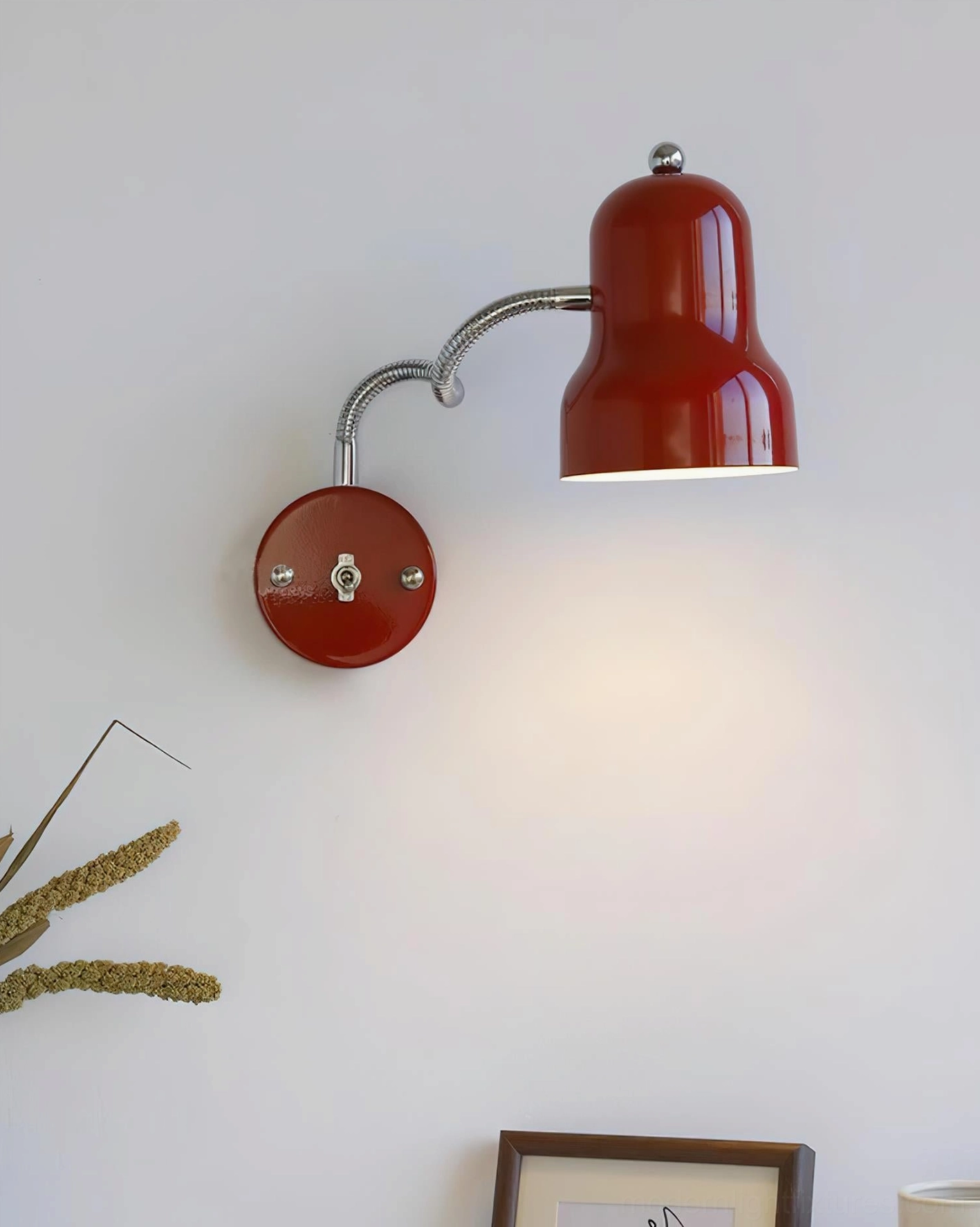Red gooseneck wall lamp mounted in minimalist interior with framed artwork and dried flowers