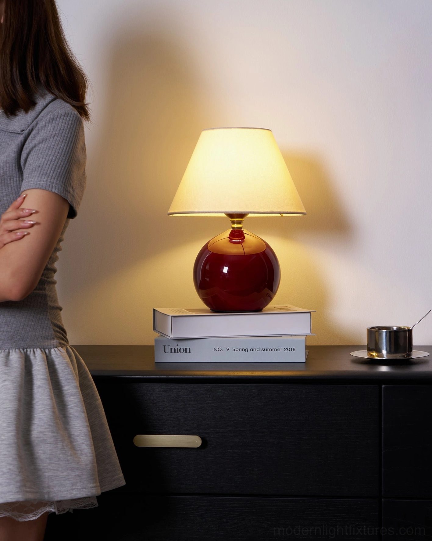 Red table lamp on bedroom dresser with cozy home ambiance, woman nearby in bedroom setting