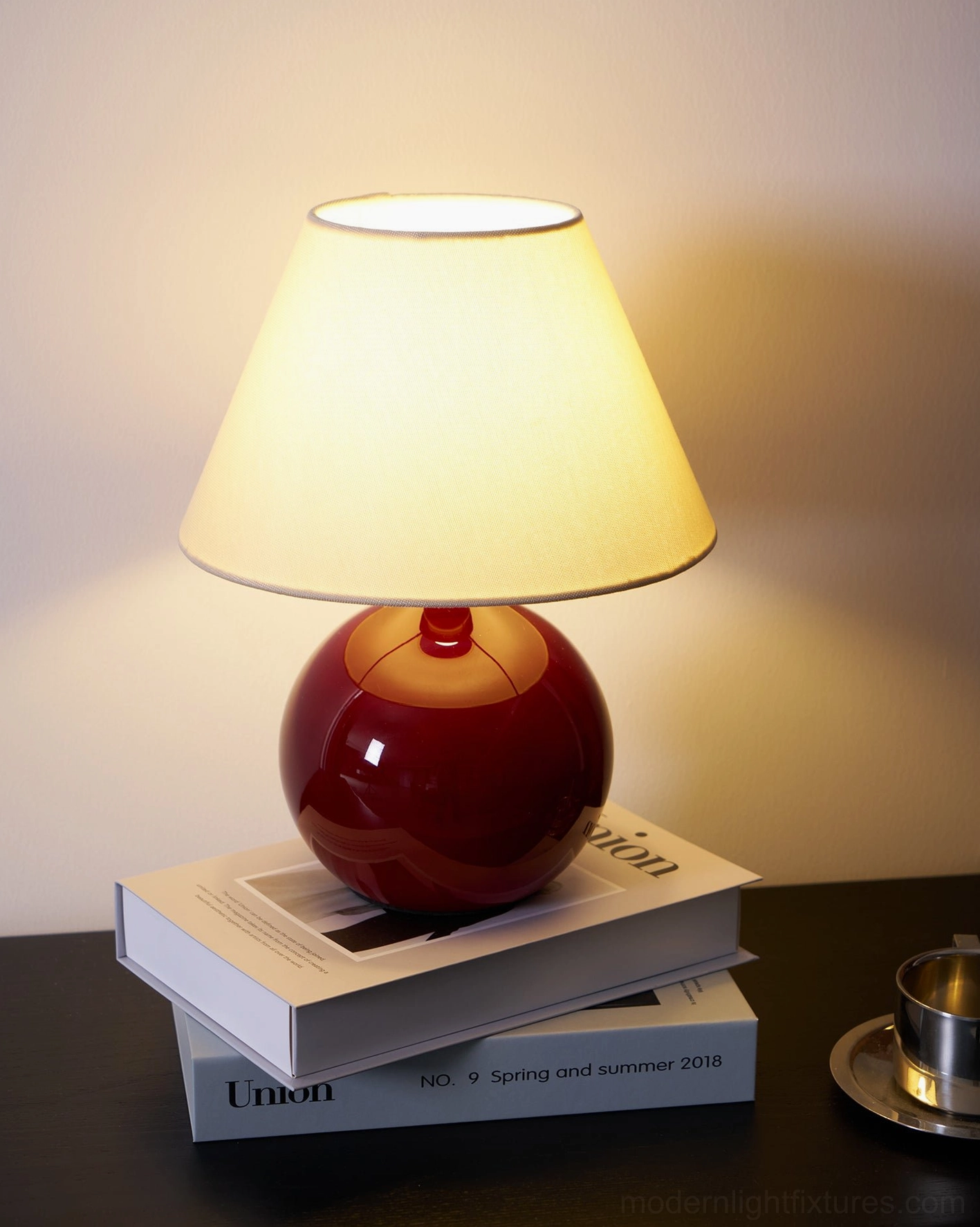Close-up illuminated view of red sphere table lamp on dark wood desk with books, intimate lighting detail