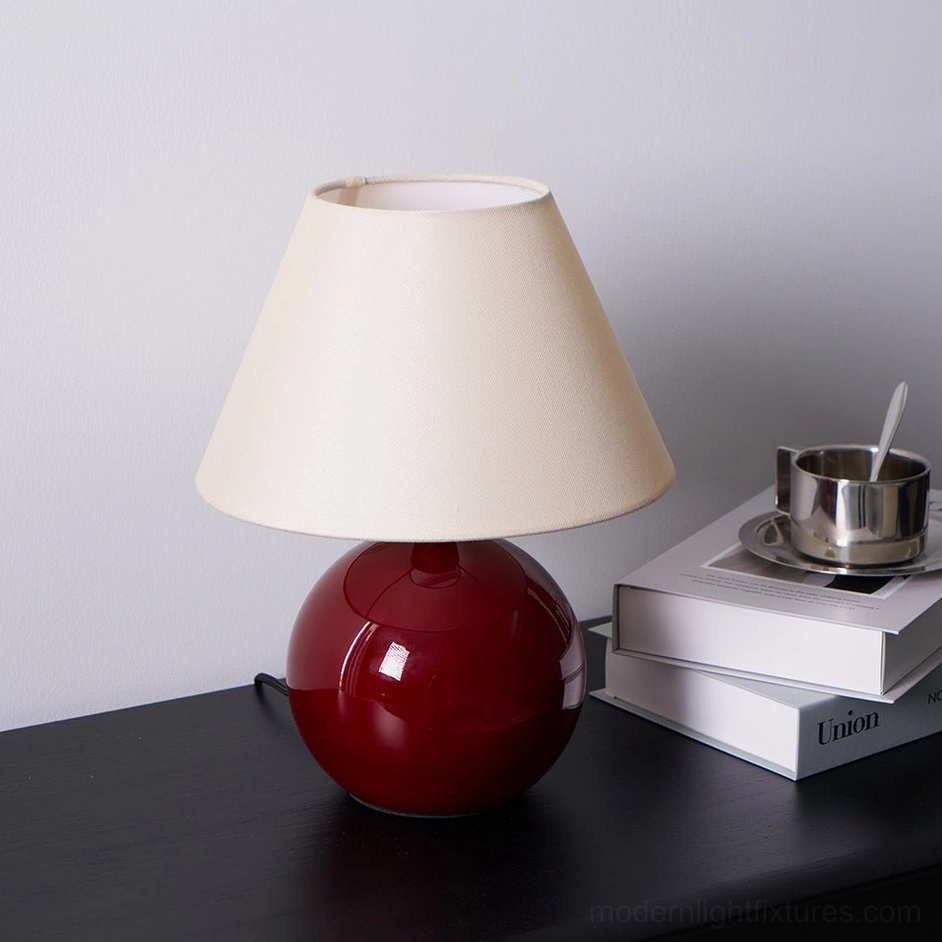 Modern red sphere table lamp with stacked books and metal cup, home interior styling arrangement