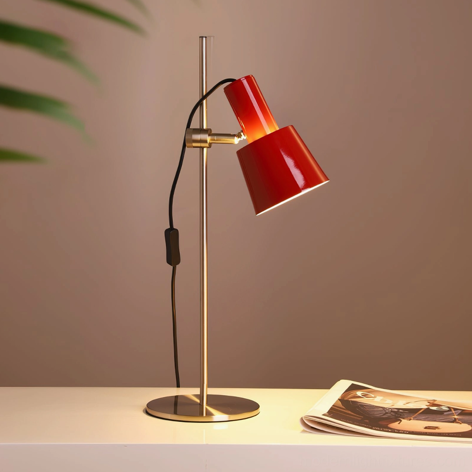 Modern dark red adjustable table lamp with warm glow displayed three-quarter view on tabletop with magazine