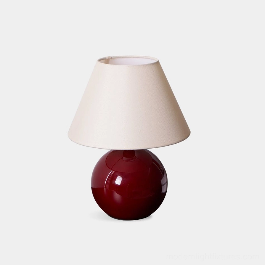 Red spherical glass table lamp with beige fabric shade on white studio background, modern minimalist design