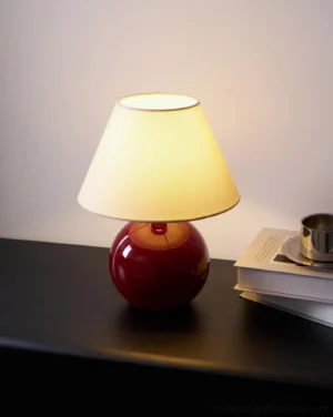 Illuminated red table lamp on dark wood bedside table, warm ambient lighting through fabric shade