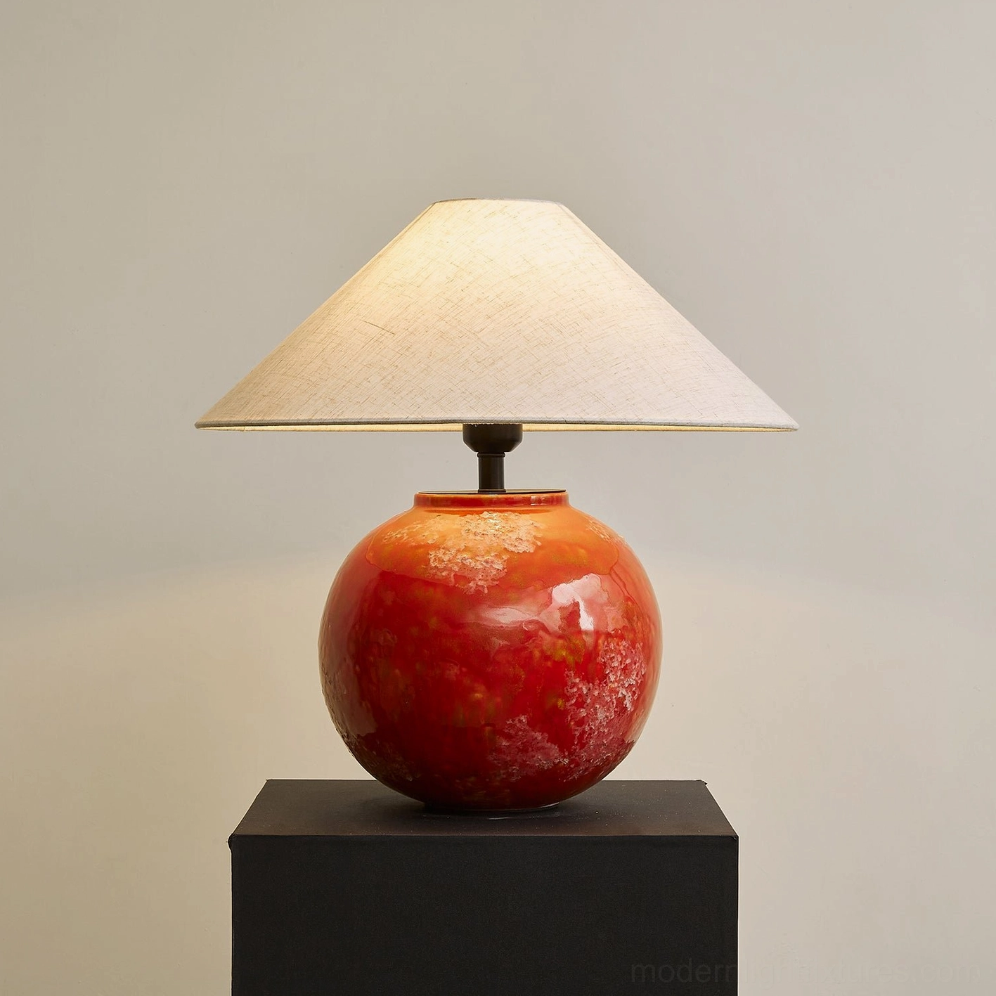 Illuminated red marbled ceramic table lamp casting warm glow from linen shade, three-quarter perspective warm studio backdrop