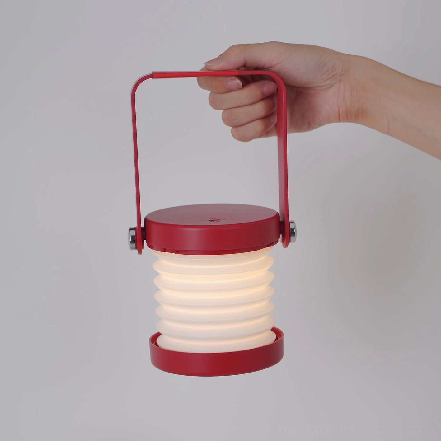 Red Terna Portable Lantern Lamp - Front view with hand gripping integrated handle showing fully visible folded accordion lamp shade