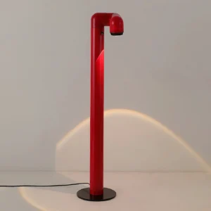 Red tubular floor lamp illuminated, casting warm focused spotlight beam, front view showing powered LED lighting and black power cord