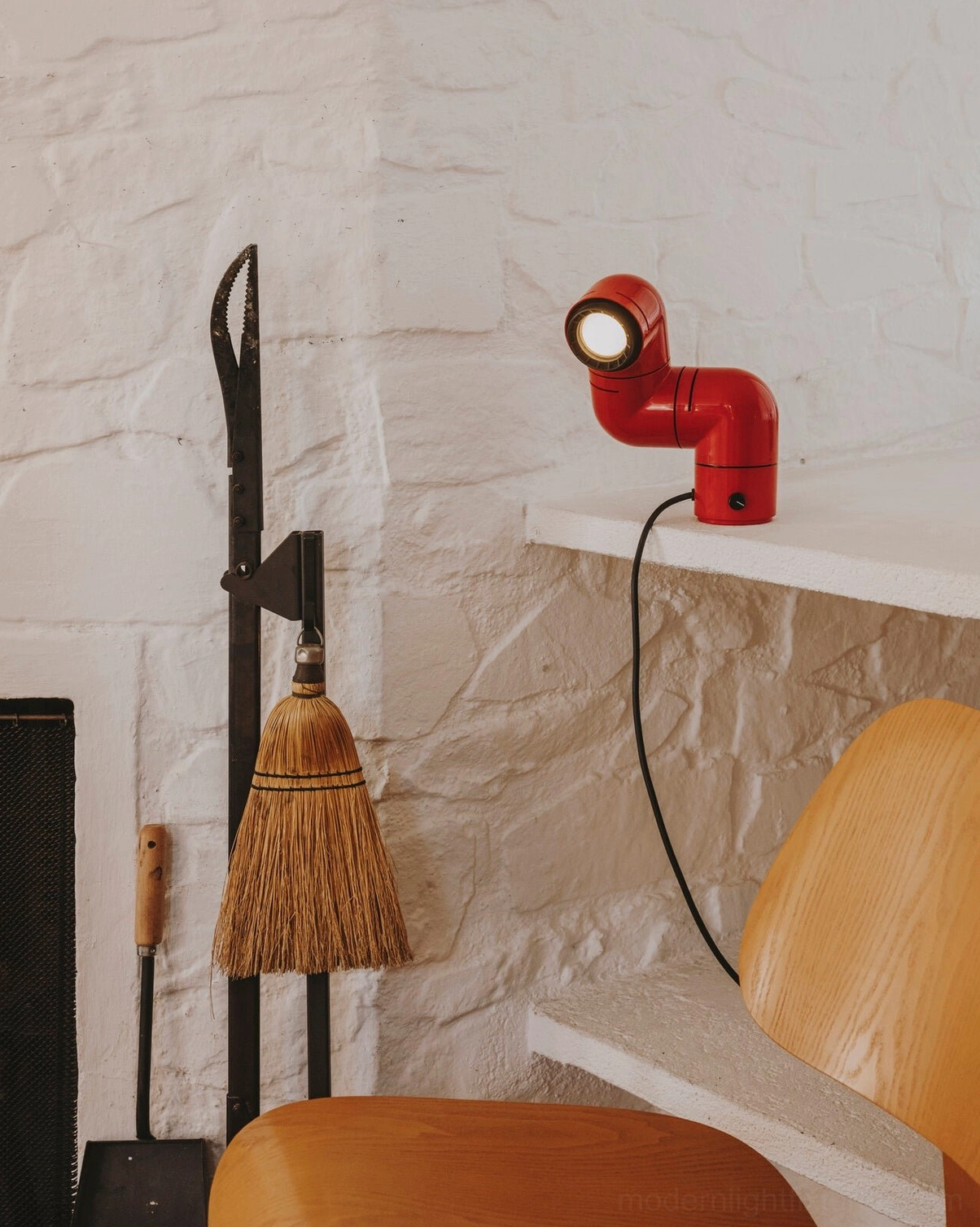 Red tubular industrial table lamp in rustic entryway corner with stone wall backdrop