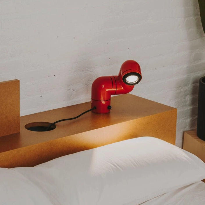 Red tubular table lamp on bedroom nightstand casting focused light beam