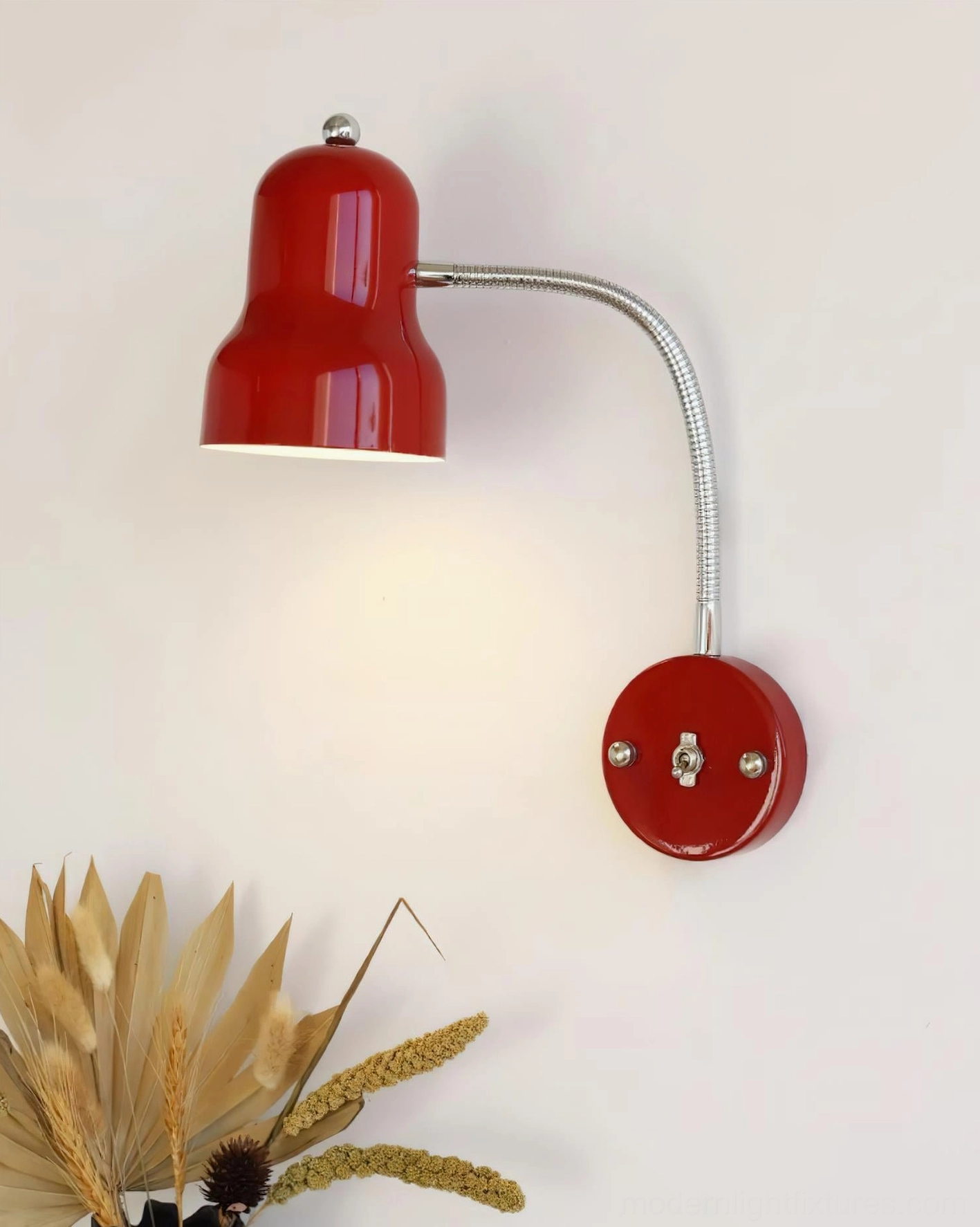Red industrial wall sconce illuminated on bedroom wall with warm lighting and metallic details