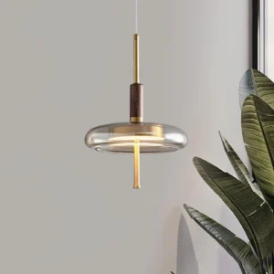 Redondo brass pendant light three-quarter view with tropical plant, displaying walnut wood joint and extended brass suspension rod