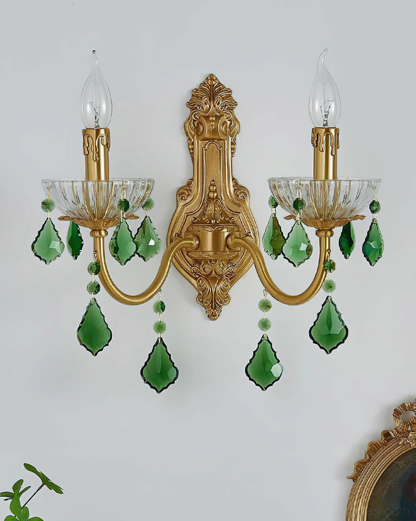 Dual candle brass wall sconce with emerald crystal pendants in styled interior with decorative frame