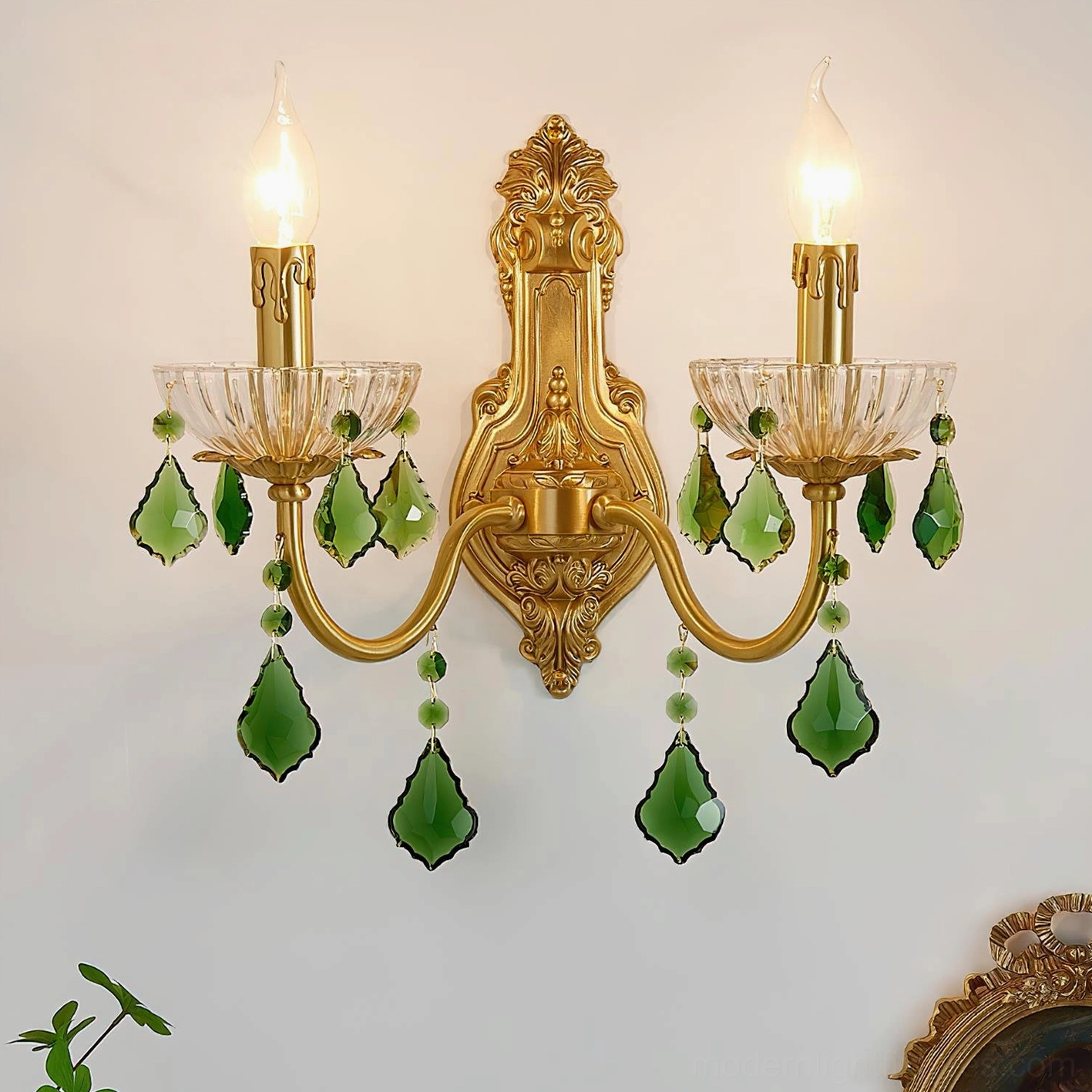 Lit dual candle brass wall sconce with hanging green crystal pendants in vintage interior setting