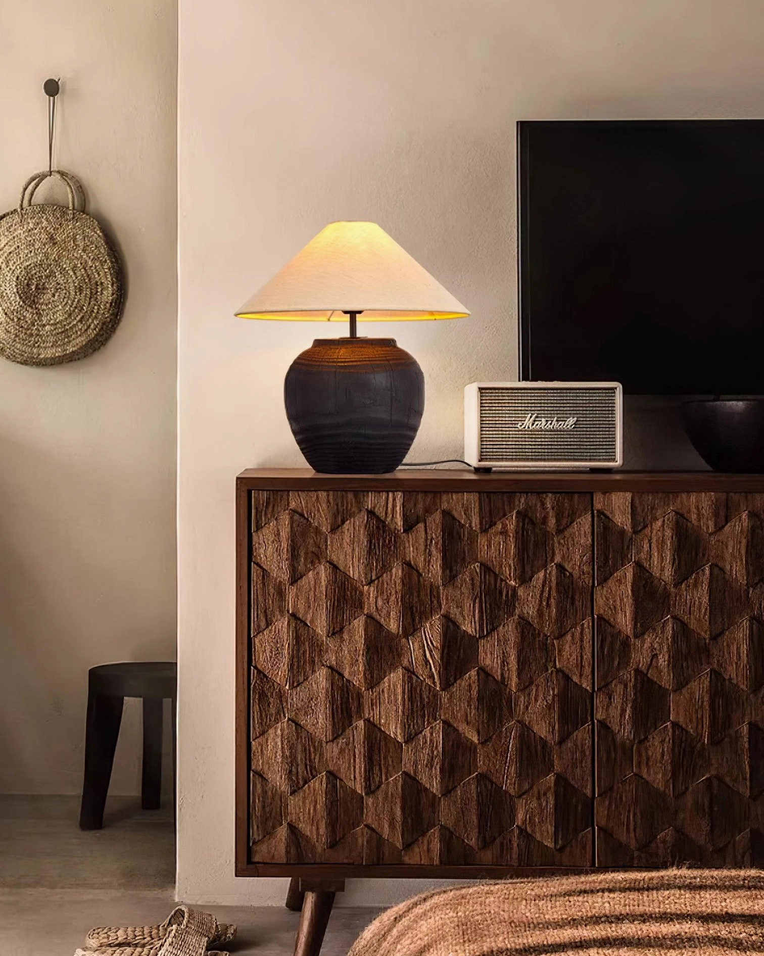 Textured black resin table lamp on patterned wood cabinet near retro speaker