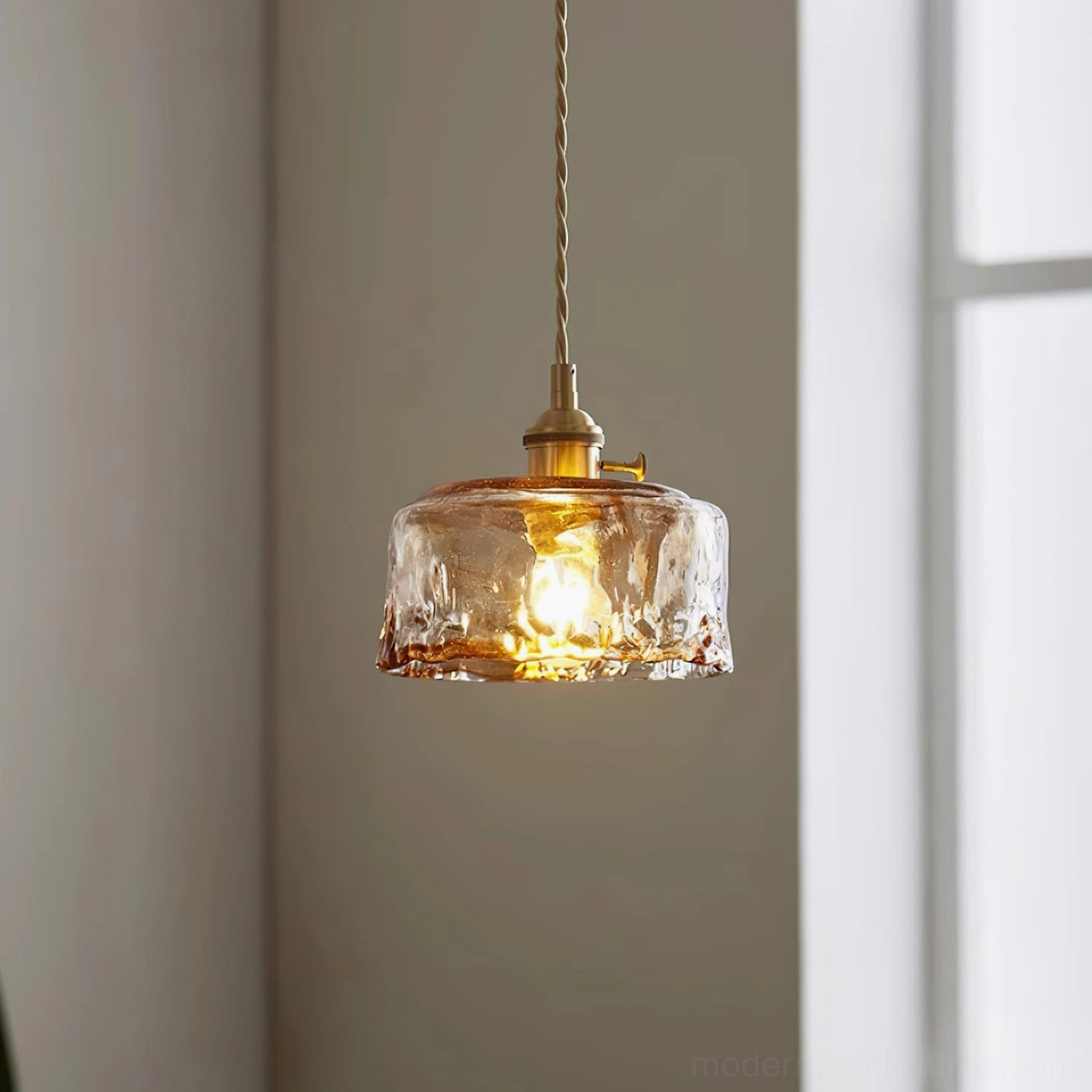 Retro hanging pendant lamp by window with warm glowing amber glass and twisted brass cord