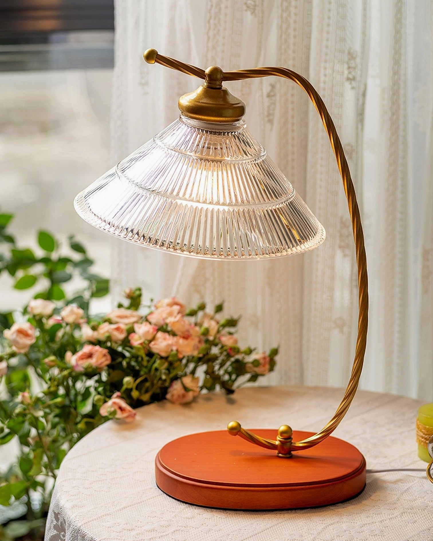Retro arc table lamp with twisted brass metal arm and tiered fluted glass shade beside pink flower bouquet on bright indoor side table