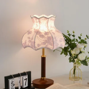 Retro pink floral table lamp with scalloped edge shade and walnut wood base, displayed on home desktop with flower vase
