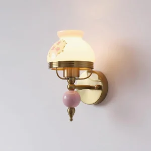 Lit vintage wall sconce with warm glowing pink frosted glass shade and brass frame, direct front view