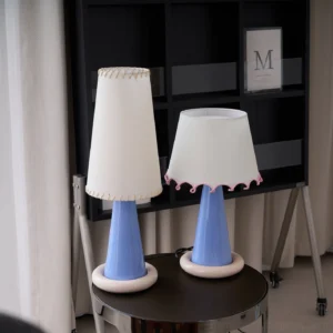 Two matching ribbon ceramic table lamps with blue gradient bases, one with pink ruffled trim and one with stitched trim, home interior setting