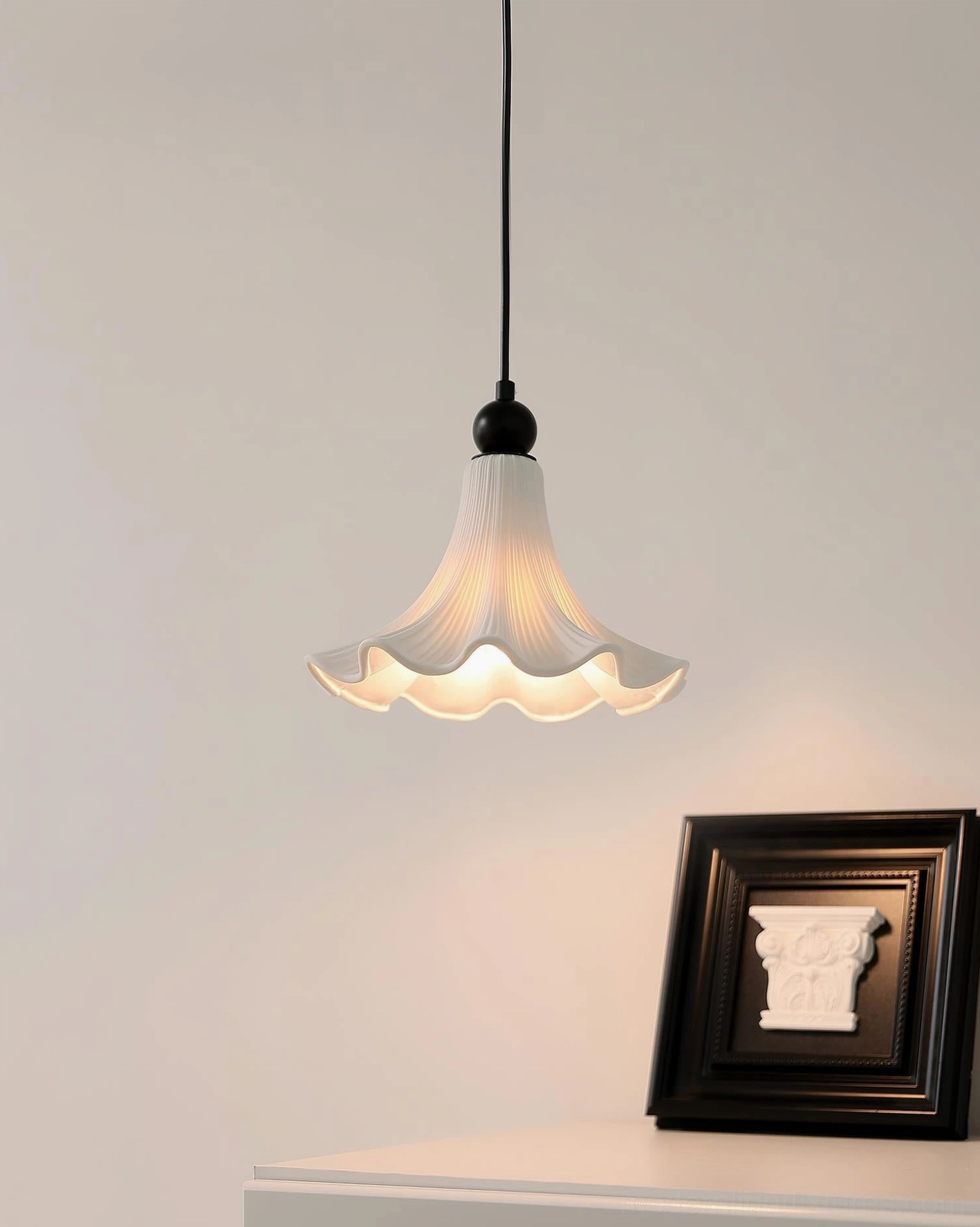 Florin Ripple pleated ceramic pendant light illuminated beside decorative wall frame in home table corner setting, warm atmospheric glow