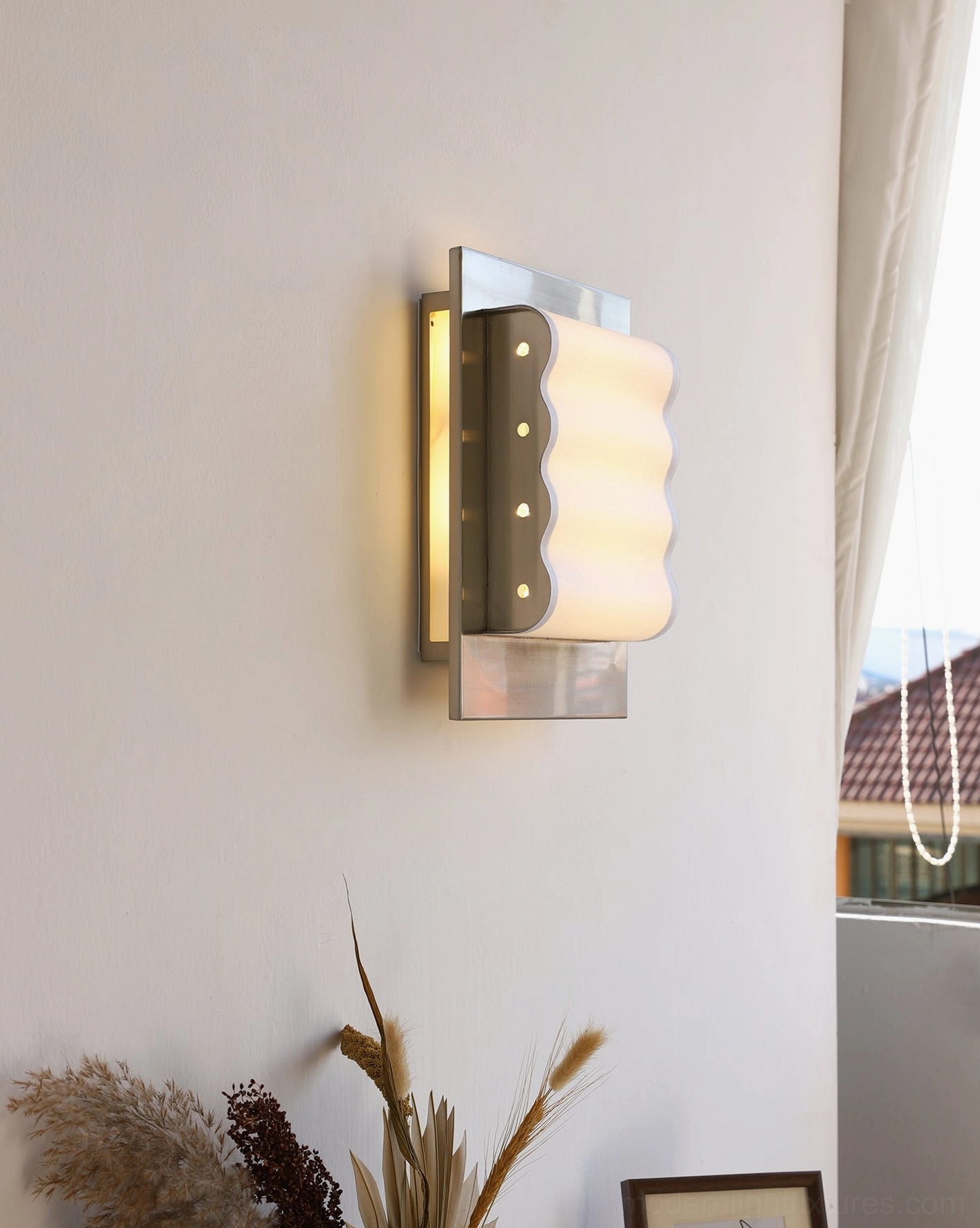 Wavy wall sconce installed on residential wall with silver metal frame and illuminated wavy shade accent lighting
