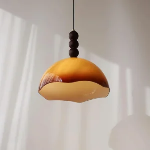 Three-quarter view of wavy-edge amber glass pendant light showing walnut bead detail and brass hardware in natural sunlight