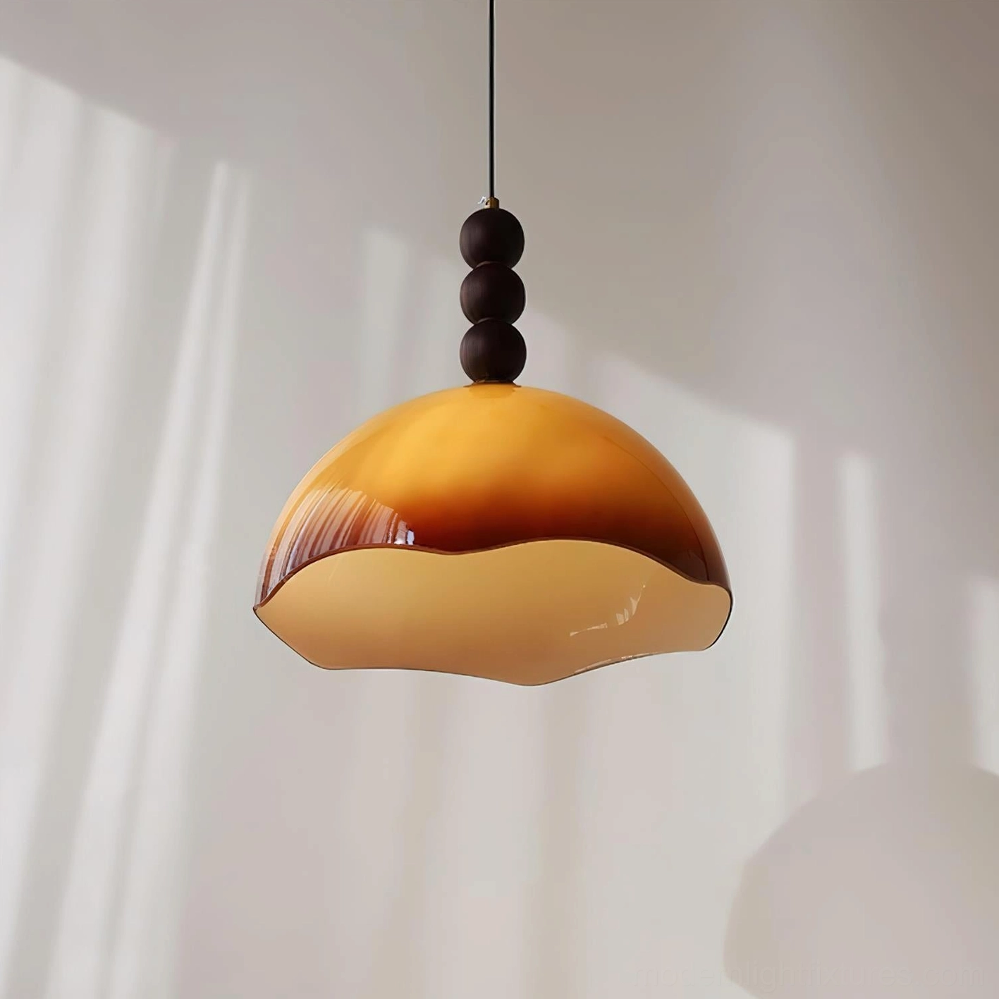 Three-quarter view of wavy-edge amber glass pendant light showing walnut bead detail and brass hardware in natural sunlight