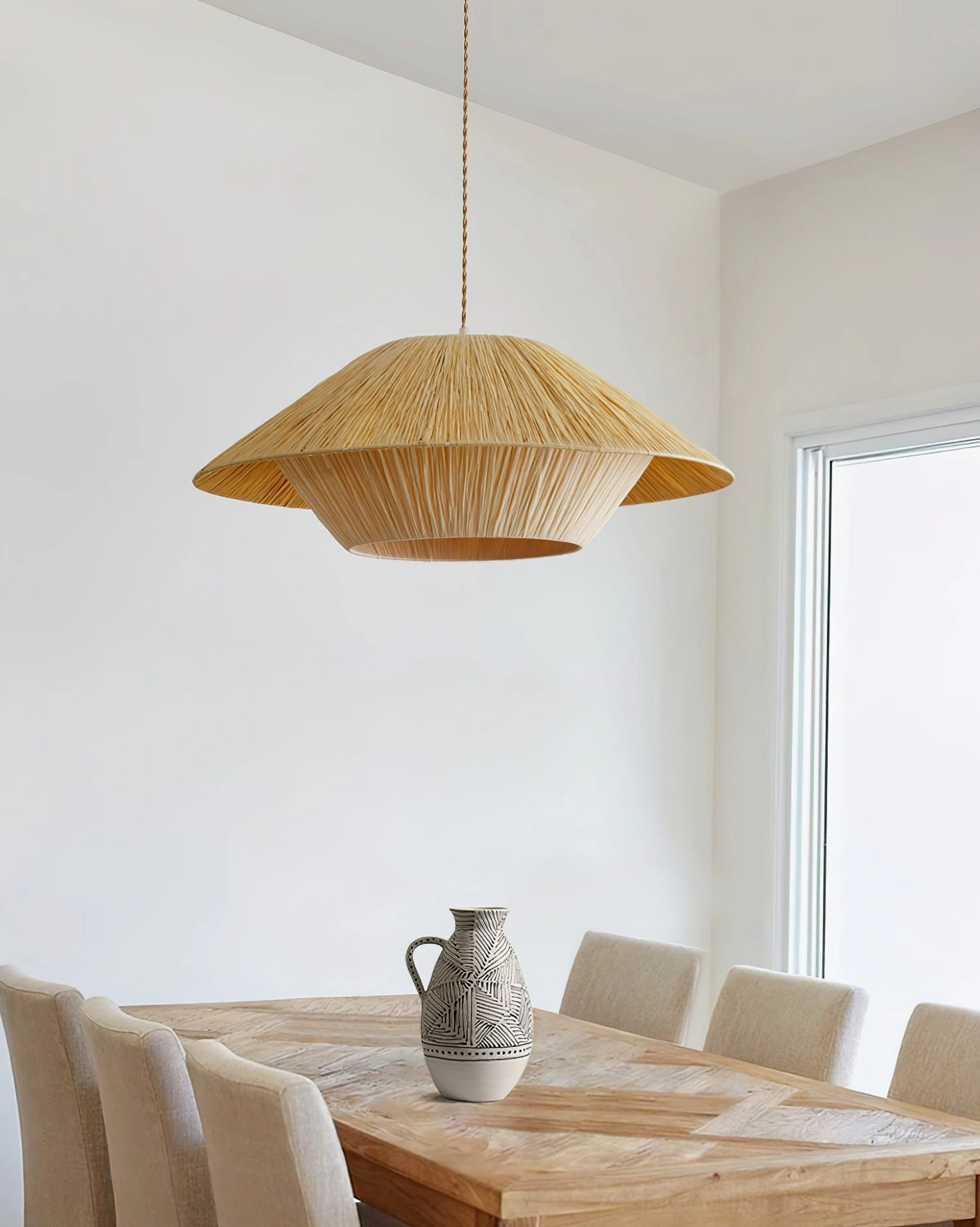 Natural raffia pendant lamp suspended over wooden dining set showing warm ambient lighting effect