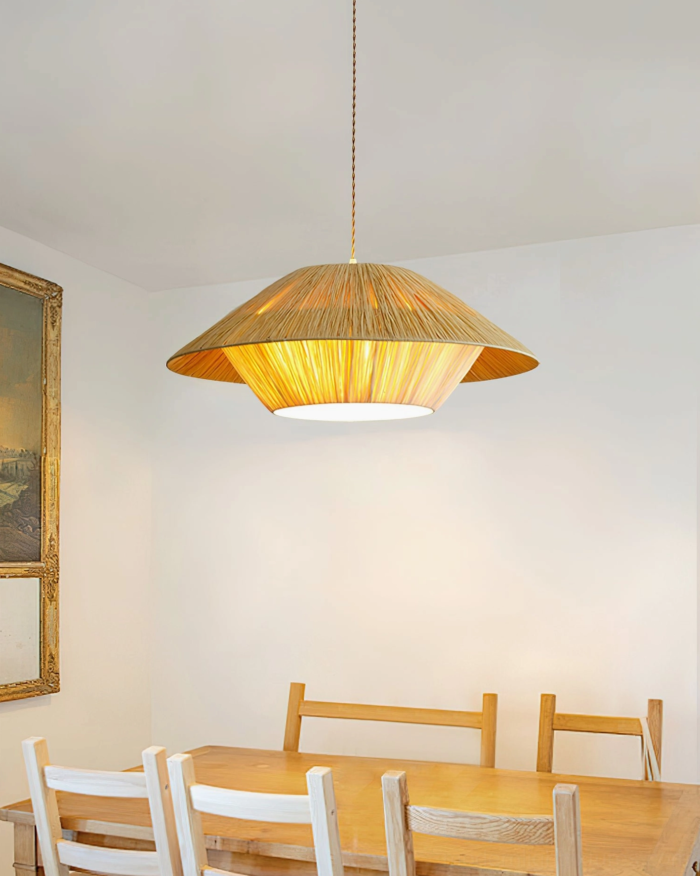 Illuminated Rivora natural raffia pendant light glowing warm above wooden table in dining room setting