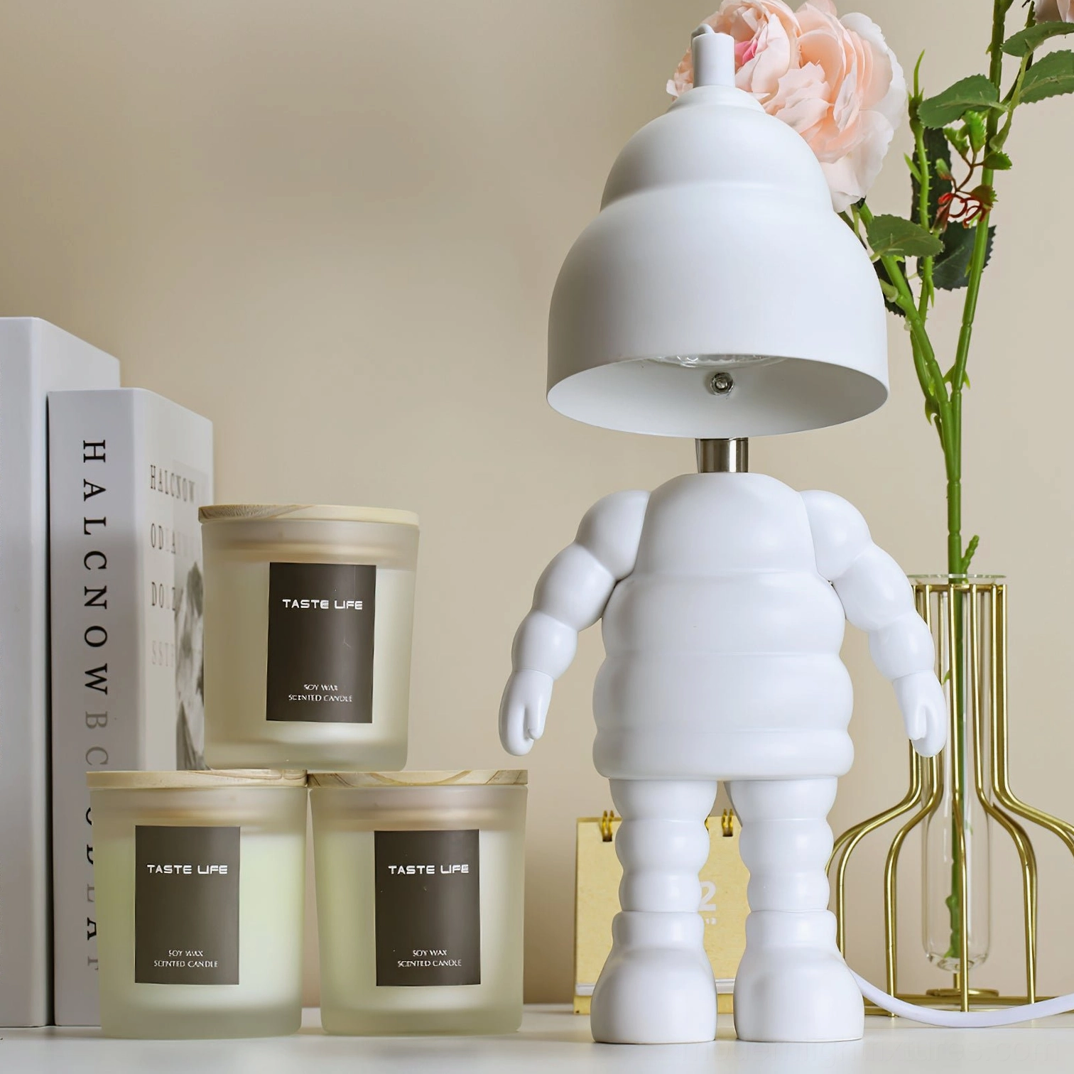 Robot-shaped wax warmer lamp displayed on home desk with books and scented candles, three-quarter perspective