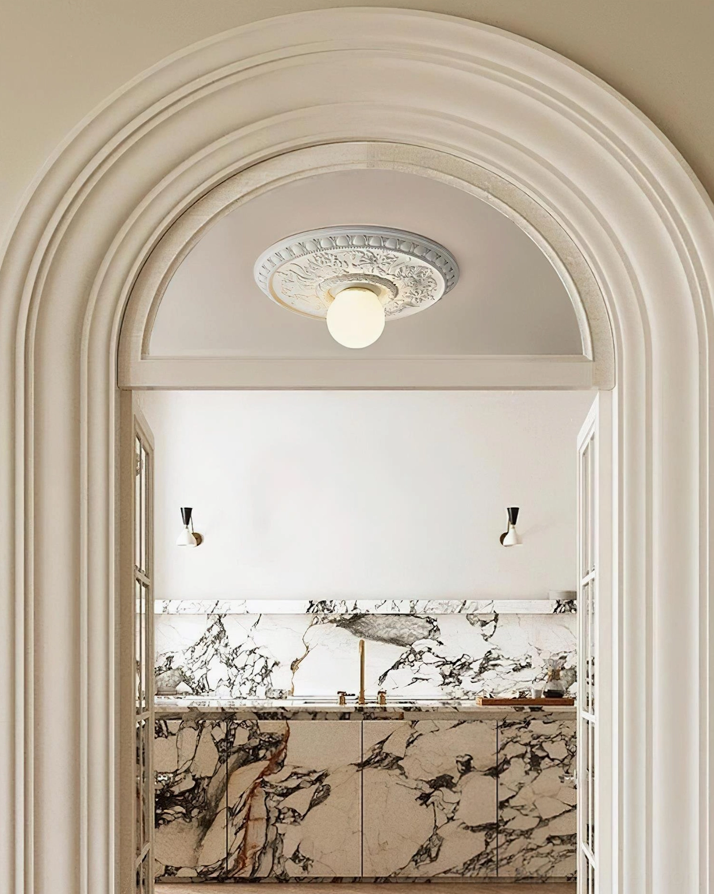 Rochelle carved ceiling light fixture viewed through archway in kitchen with marble and neutral tones