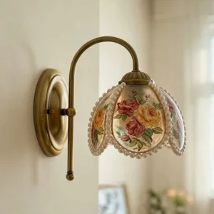 Rosabelle brass wall sconce installed in residential bedroom, showing side profile with antique gold finish and rose-patterned resin shade