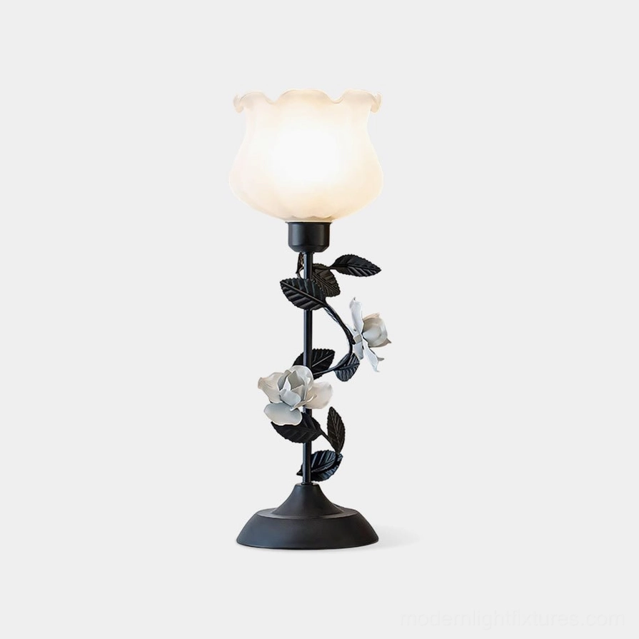 Roselith floral table lamp with black wrought iron stem and frosted white glass shade adorned with rose blossom decorations, front view studio shot