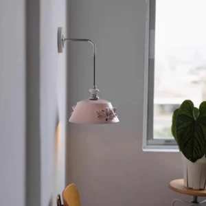 Ceramic wall lamp Roselune with pink flower-decorated shade and curved silver metal arm in Nordic minimalist home interior