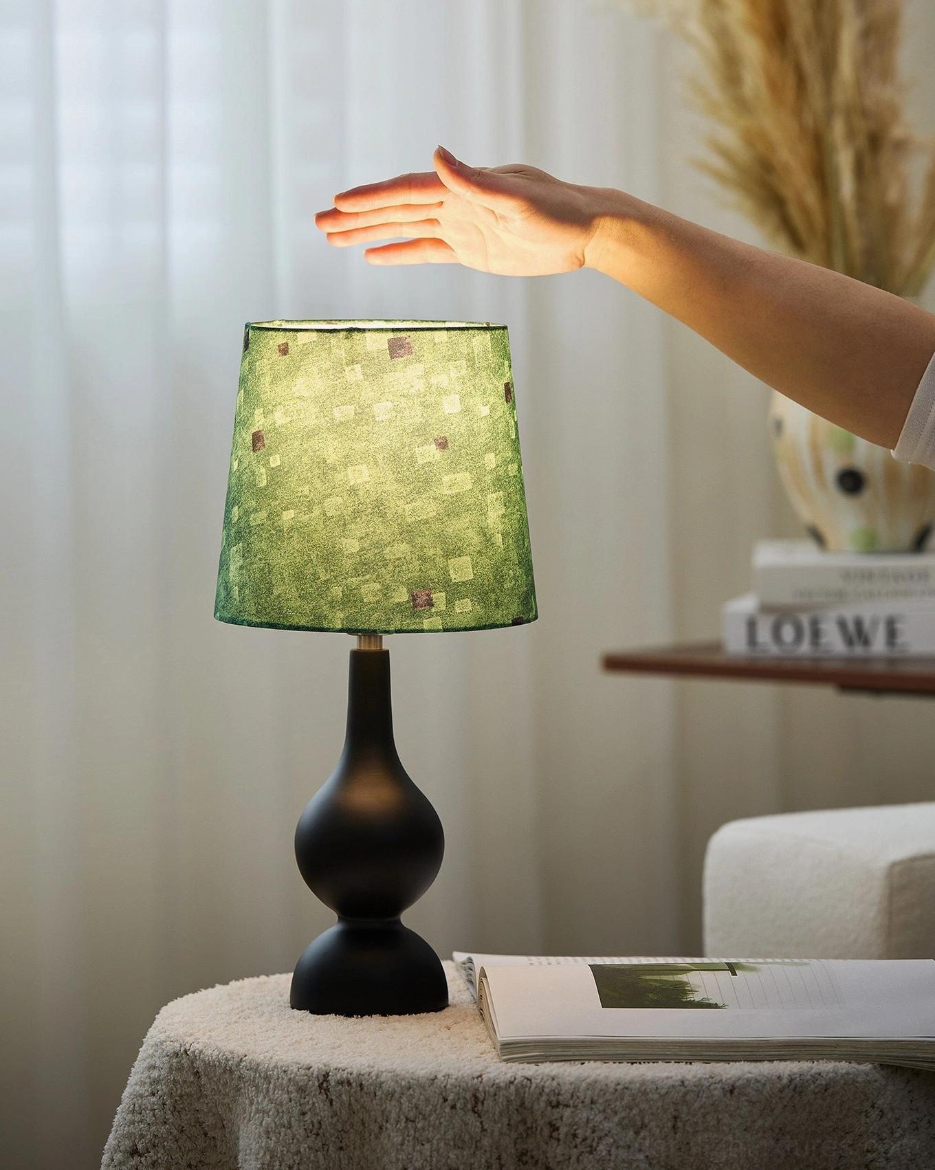 Japandi mid-century table lamp with green checkered fabric shade, hand touching base, living room console