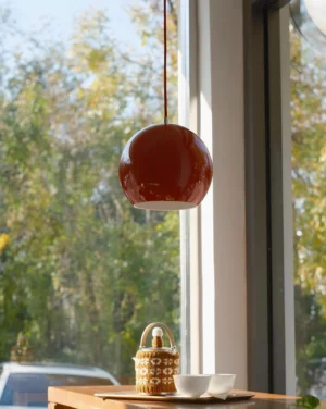 Burgundy red Rosso Dot pendant lamp suspended over dining table with natural window light - contemporary interior design