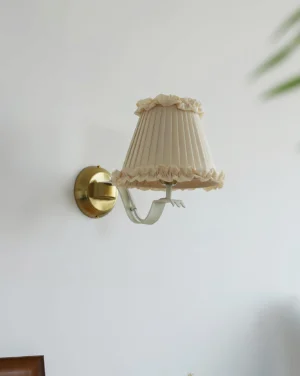 Pleated fabric wall lamp with brass base mounted on white wall, side angle showing cream shade