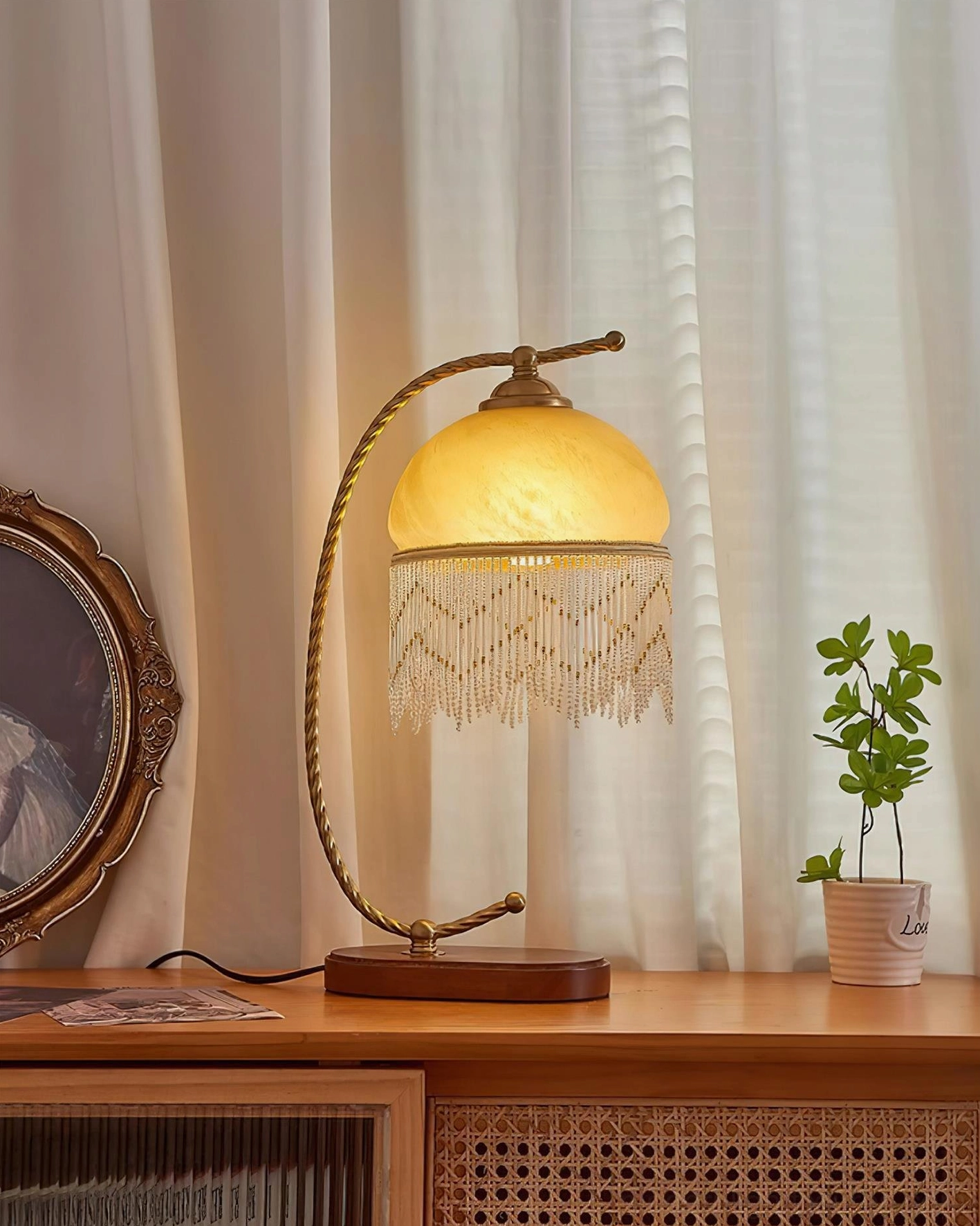 Lit Roussillon Tassel Table Lamp glowing warm yellow light frosted glass shade on vintage dresser with potted plant mirror