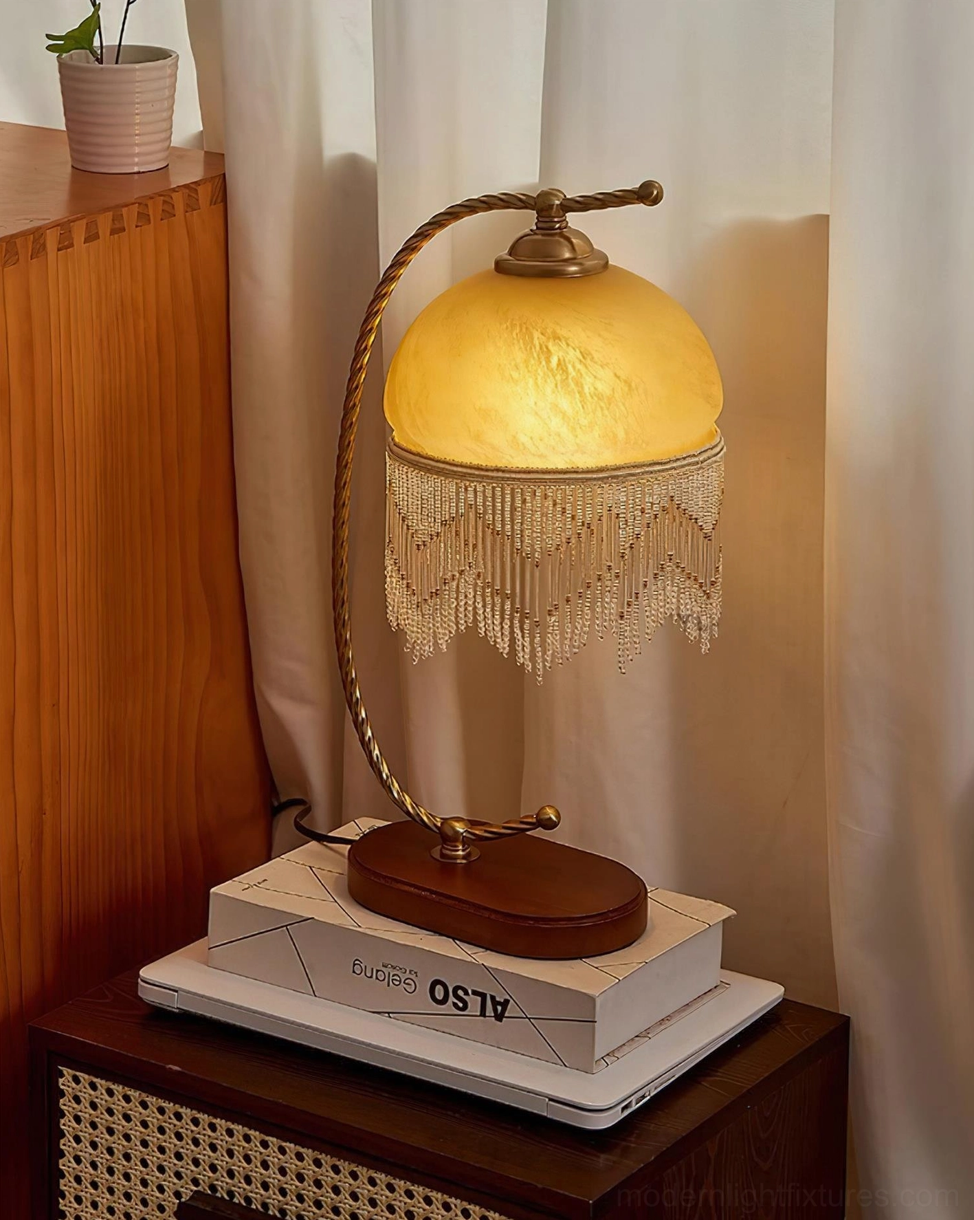 Roussillon Tassel Table Lamp lit yellow shade three-quarter view on vintage books stack warm ambient lighting