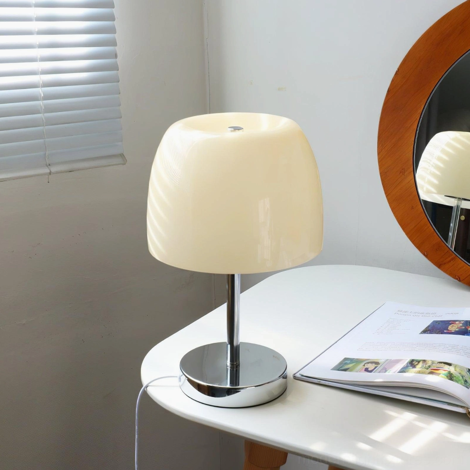 Modern matte off-white glass table lamp on dresser with round mirror and magazines