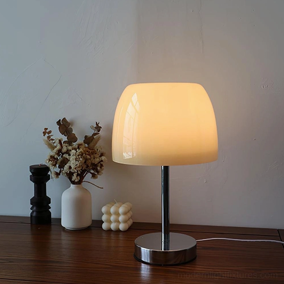 Lit off-white glass table lamp providing warm ambient lighting on dark wood desk